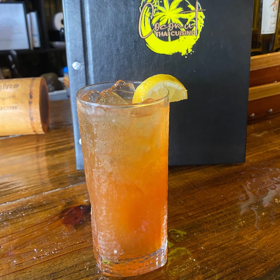 Iced tea with a lemon wedge on a wooden table, with a "Coconut Thai Cuisine" menu in the background.
