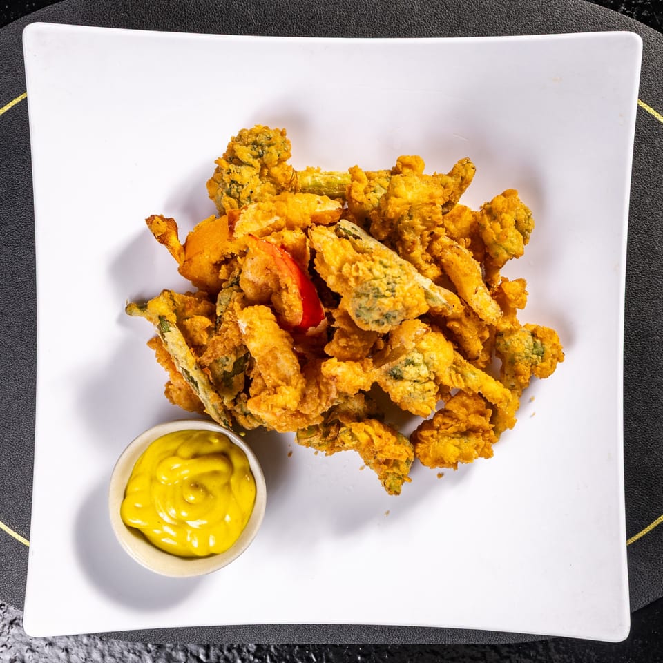 Crispy fried vegetables, including broccoli and red pepper, served with a side of yellow mustard.