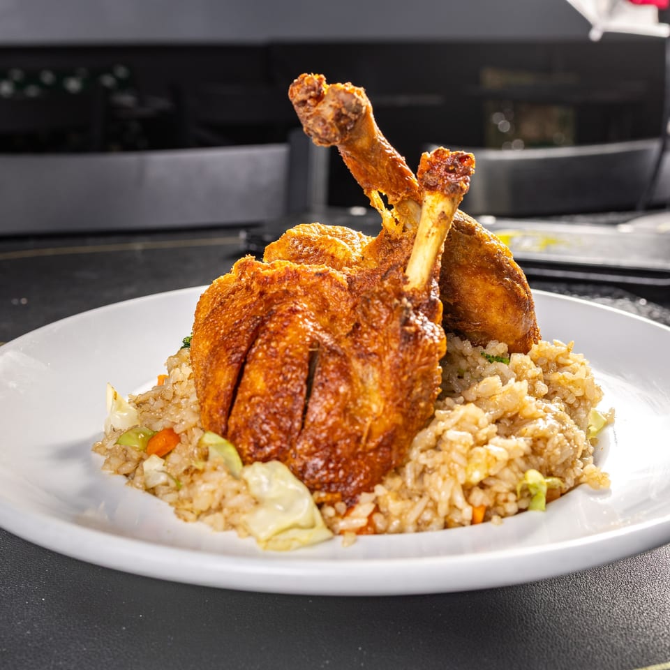Crispy fried chicken drumsticks and thighs served over a bed of vegetable fried rice on a white plate.
