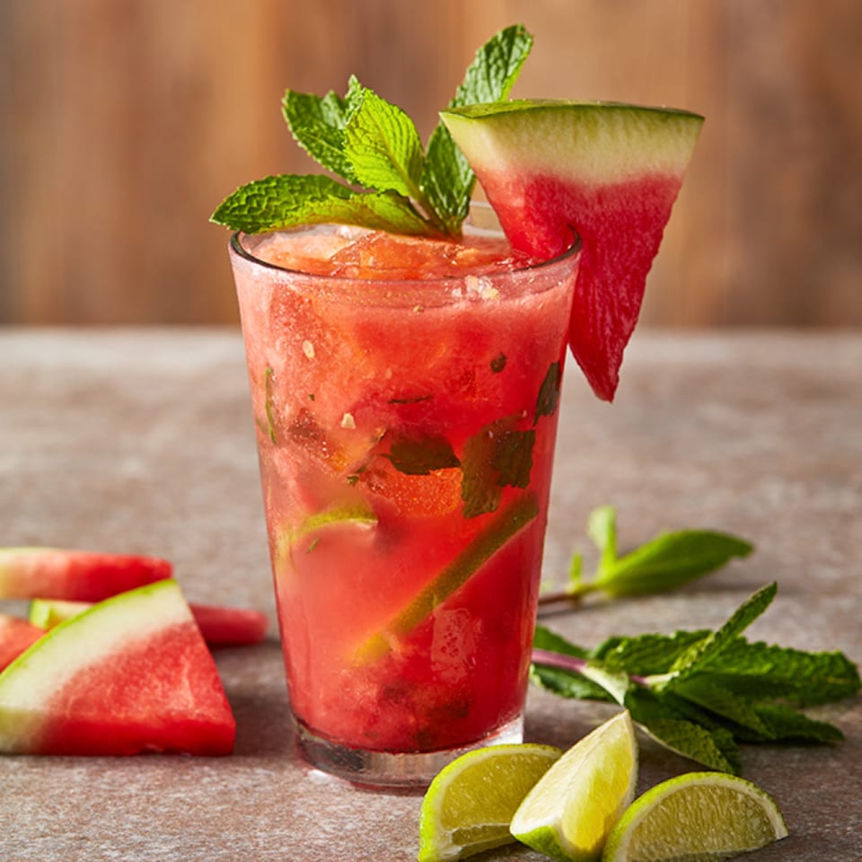 Refreshing watermelon mojito garnished with mint and a watermelon slice, surrounded by lime wedges.