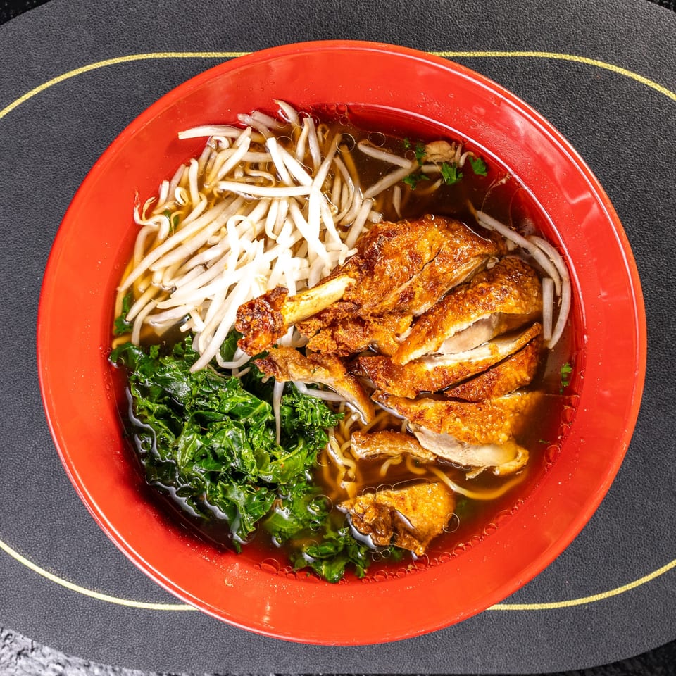 Crispy duck ramen in a red bowl, with bean sprouts, kale, and rich broth.